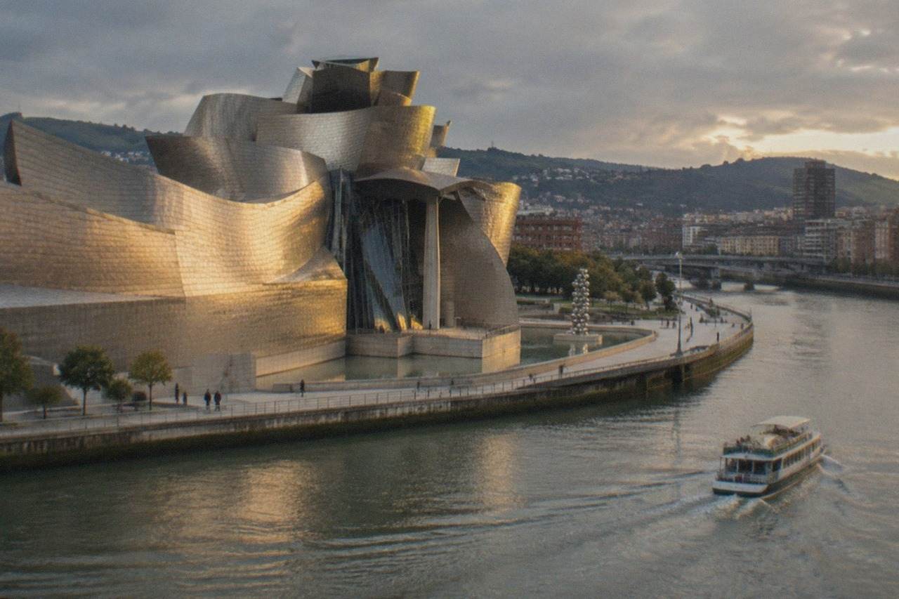 A boat cruising on the Bilbao estuary with the Guggenheim Museum and riverside promenade in view