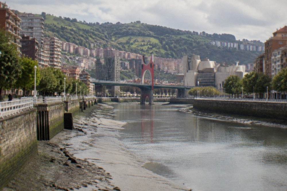 View across the Bilbao estuary at low tide showing stone embankments and the Salve Bridge in the distance