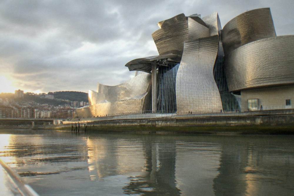 The Guggenheim Museum's titanium curves seen from a boat on the estuary with calm water reflecting the building