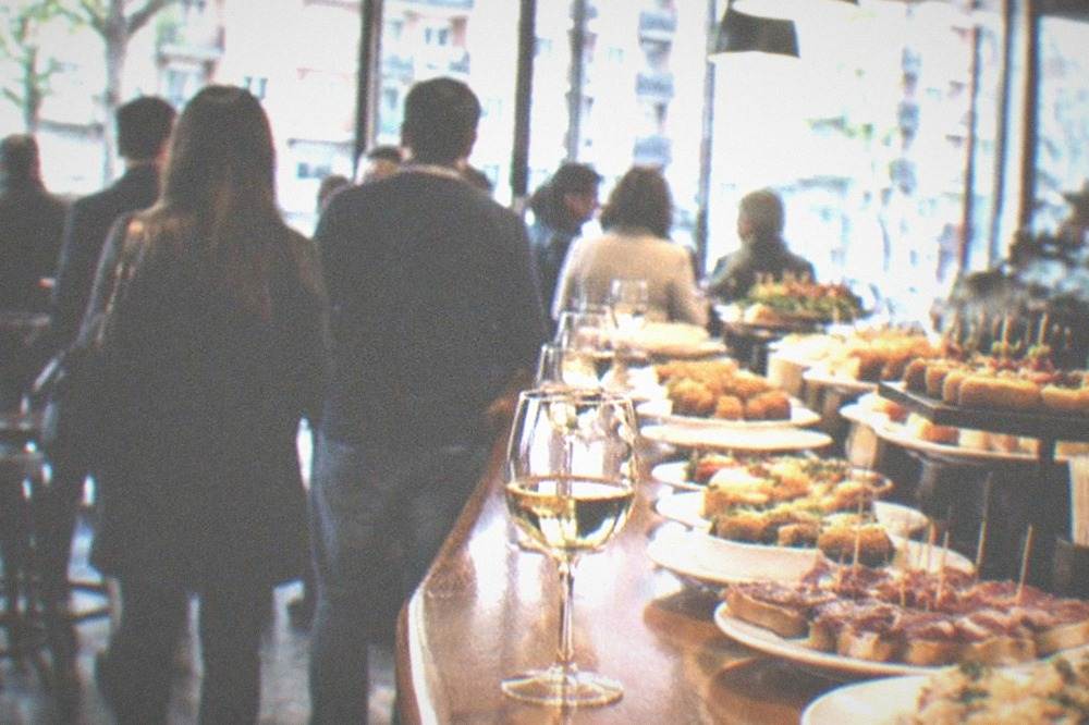 A crowded pintxos bar counter in the Indautxu district near San Mames with plates of small bites and glasses of txakoli