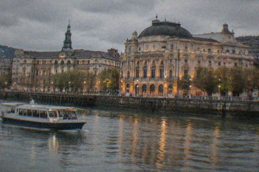 Evening view of the theatre's lit facade from across the Nervion estuary, with the town hall opposite