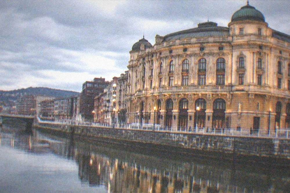 The theatre's illuminated facade reflected in the calm water of the estuary at night