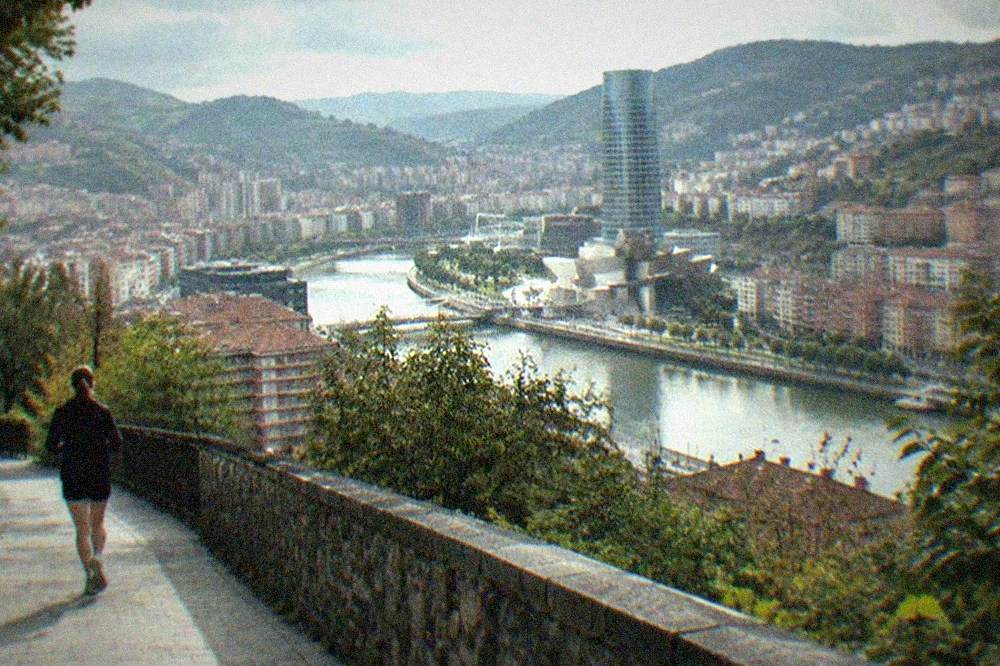 The Bilbao skyline seen from a hillside viewpoint with the glass tower and the estuary below in soft evening light