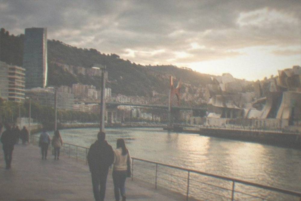 People strolling on a wide riverside promenade in Bilbao with modern architecture on both banks of the estuary