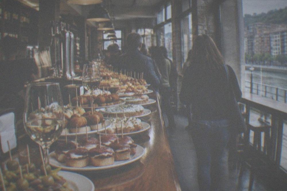 A busy pintxos bar counter in Bilbao with plates of small skewered snacks and glasses of txakoli wine