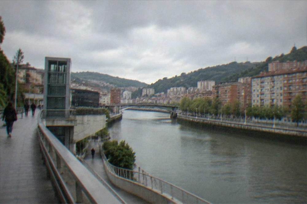 A modern pedestrian walkway in Bilbao with elevators and ramps connecting the riverfront to the street level above