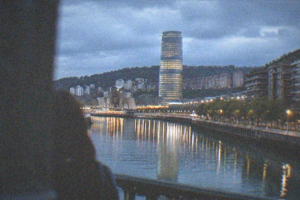 The illuminated glass tower seen at dusk from a Bilbao bridge with city lights reflecting in the estuary
