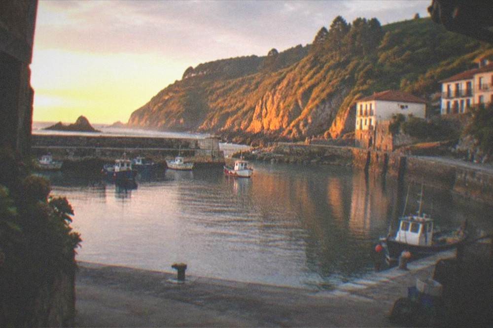 Village harbour at golden hour with calm water and warm light on the cliffs