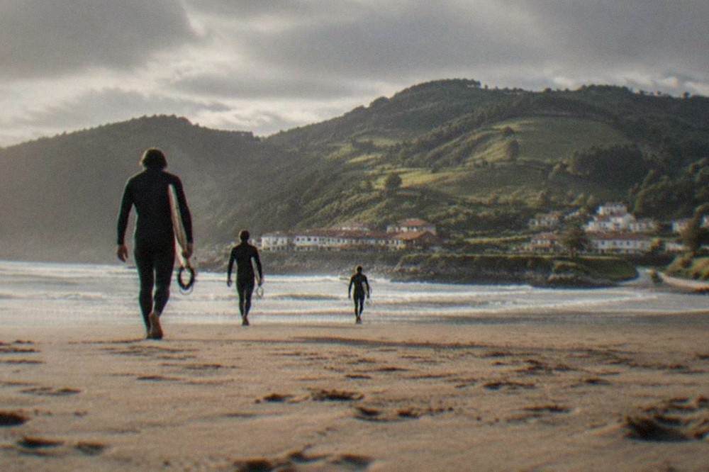 Surfers in wetsuits walking across a sandy beach toward small waves