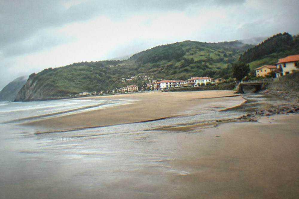 An empty sandy beach under a grey Atlantic sky with low cliffs at one end