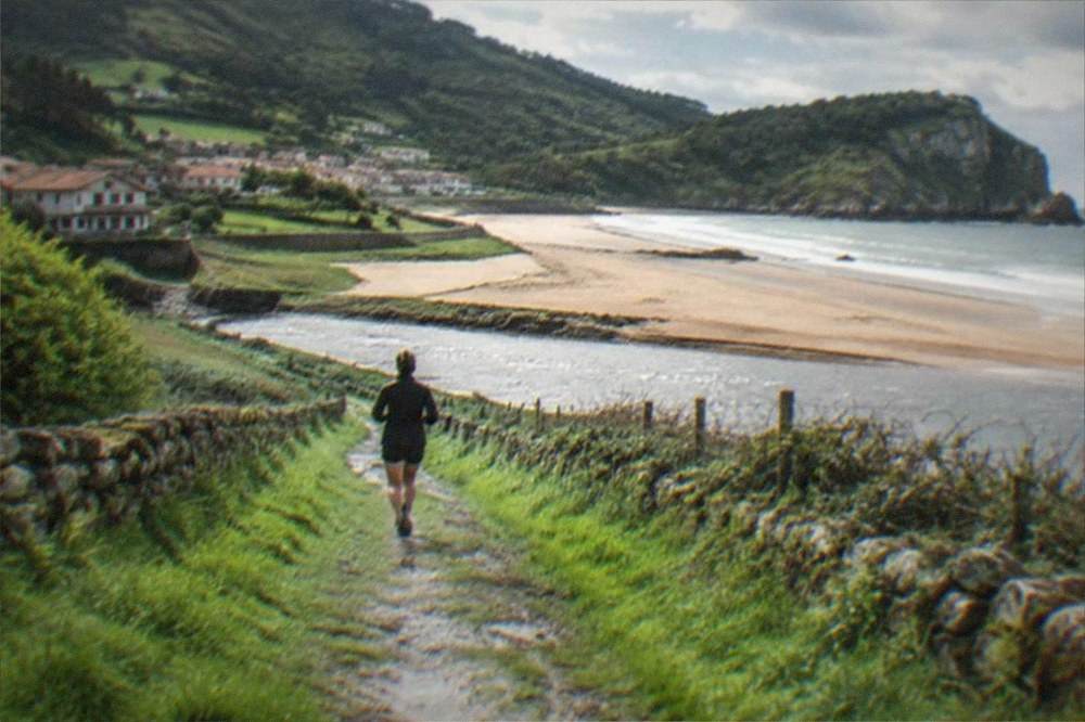 A coastal path of wet grass and low stone walls leading toward a headland