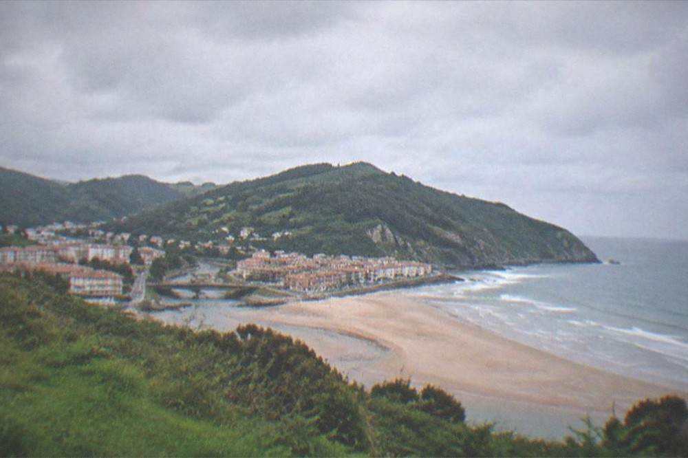 A view from a green headland over a coastal town and the open sea beyond