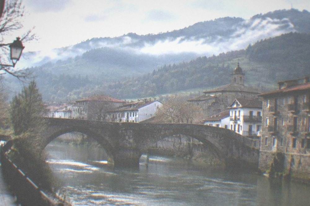 Green forested mountains with morning mist above a small town rooftops in Basque Country