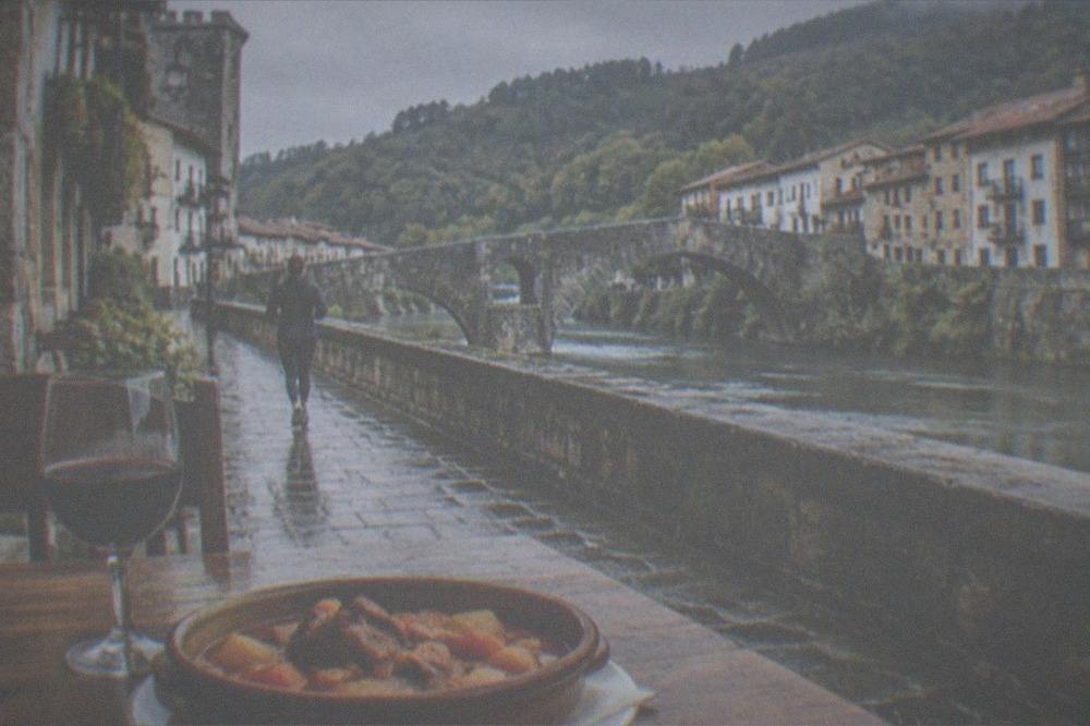 A slow-cooked Basque stew and glass of red wine served on a rustic wooden restaurant table