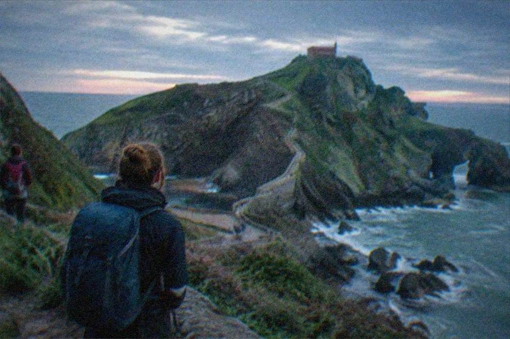 Hikers with backpacks pausing on the coastal path above the Atlantic near San Juan de Gaztelugatxe