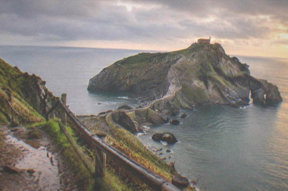 The islet of San Juan de Gaztelugatxe seen from a clifftop trail at golden hour with calm sea