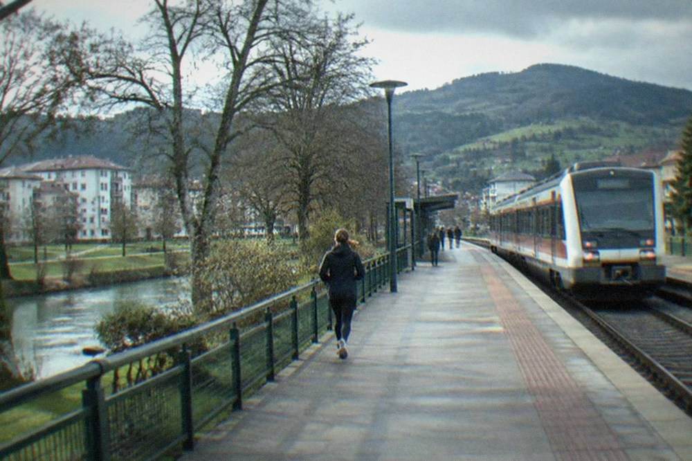 A regional train waiting at a small Basque country station with green hills behind it
