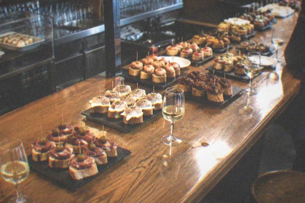 A traditional Basque pintxos bar counter with rows of small skewered snacks and glasses of txakoli wine