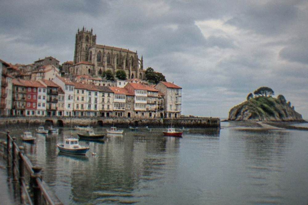 The Gothic facade of a large stone basilica above the rooftops of a small Basque town