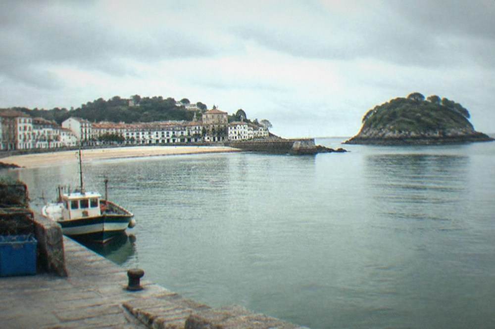 A wide sandy beach curving along a small town waterfront with a green island offshore