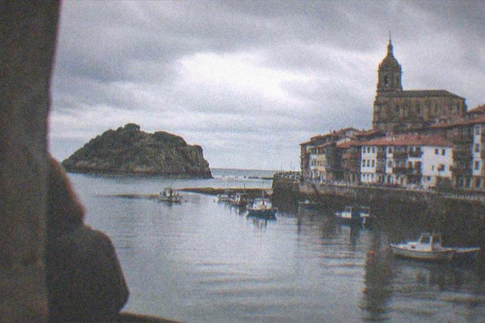 A calm evening view over a small harbour town with a basilica tower rising above red rooftops