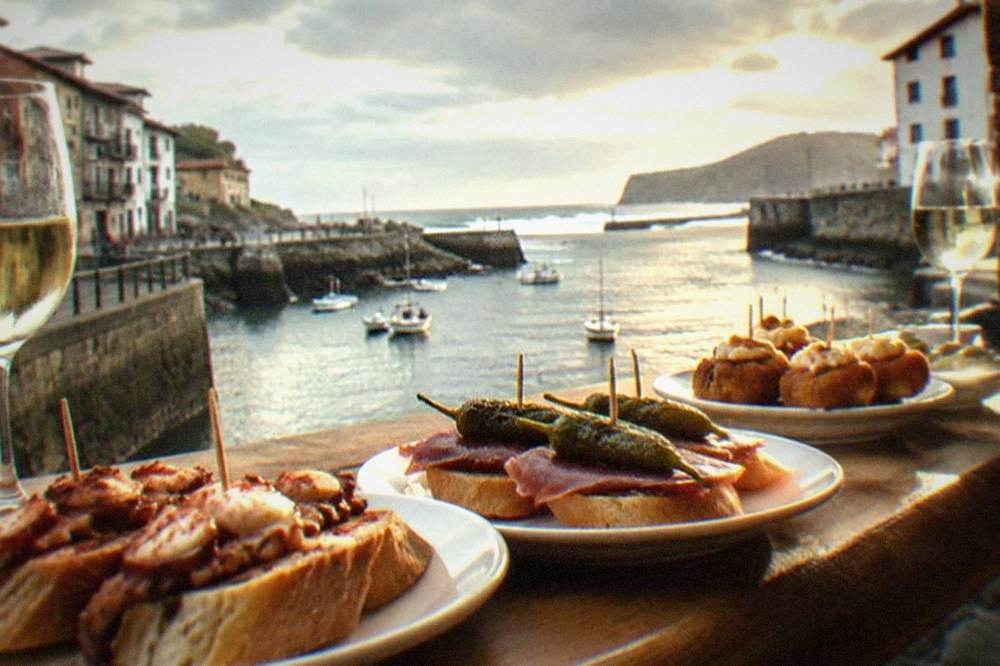 Pintxos arranged on a bar counter with glasses of pale txakoli wine beside them