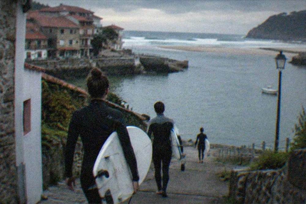Surfers carrying boards along a coastal path towards the water at a river mouth