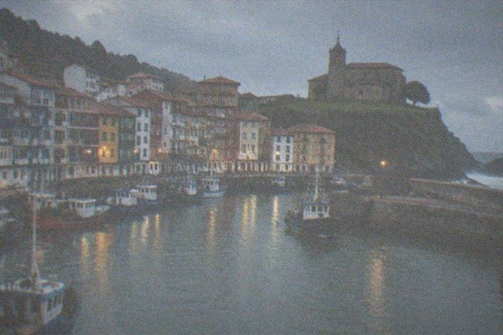 A stone church standing on a grassy cliff above a harbour with waves breaking below