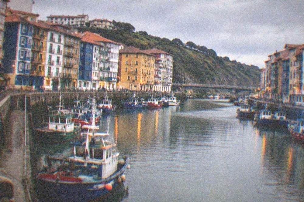 A quiet Basque harbour at dusk with warm lights reflecting on the water and boats at rest