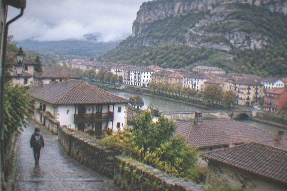 Hiker with a small backpack walking up a cobbled street in a Basque mountain town