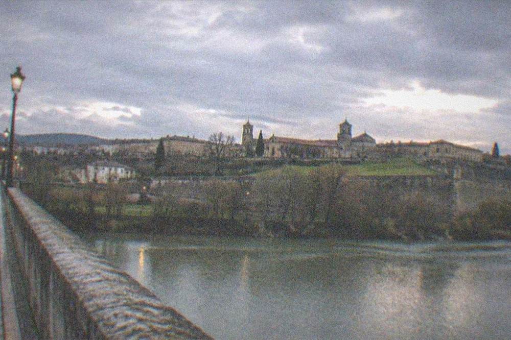 Evening light on a stone bridge over a river with a walled city beyond