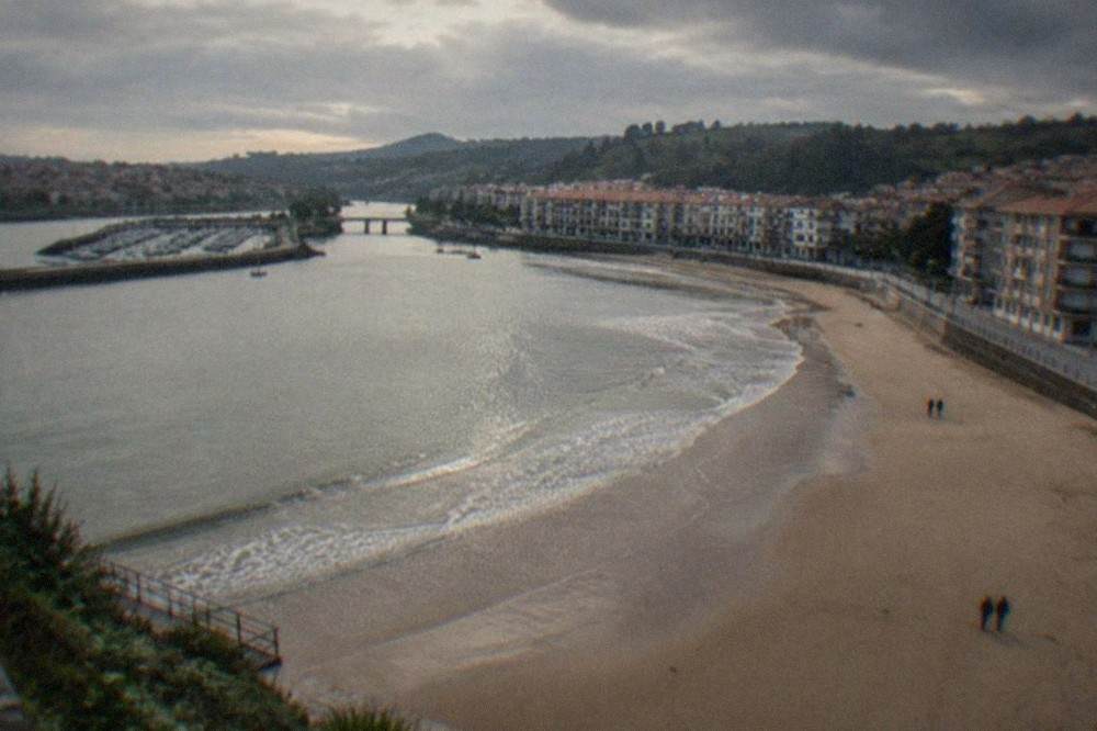 A wide sandy beach curving along a calm bay with gentle waves and a promenade