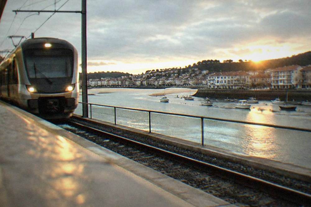A modern metro station platform with a train arriving beside a riverside setting