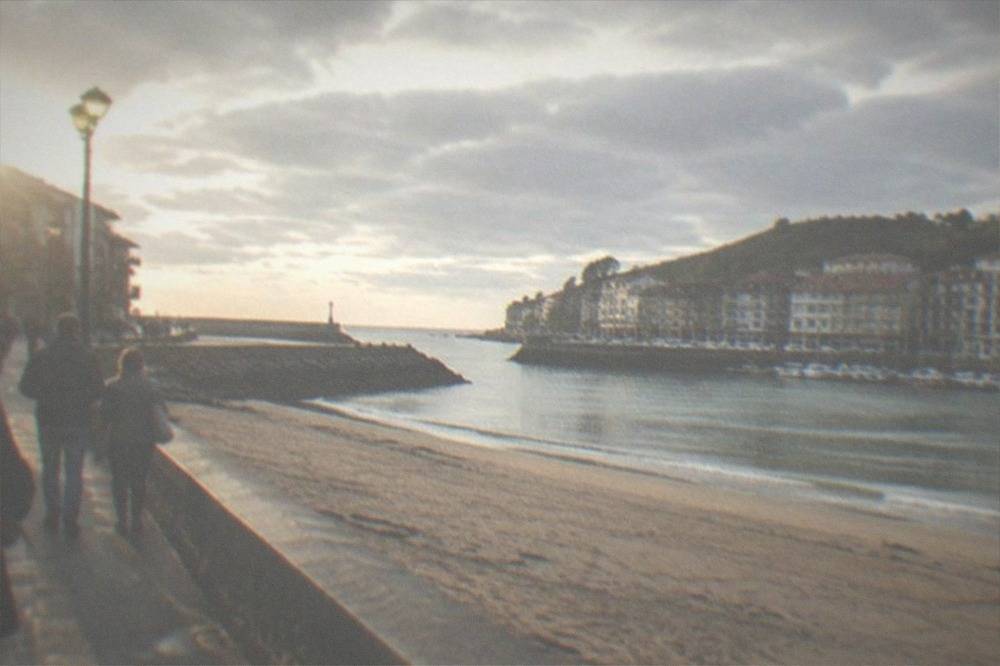 People walking a seafront promenade beside a sandy beach on a mild day