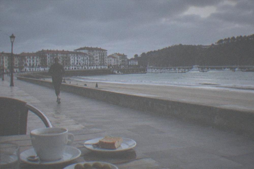 An outdoor cafe table beside a beach promenade with coffee and small plates