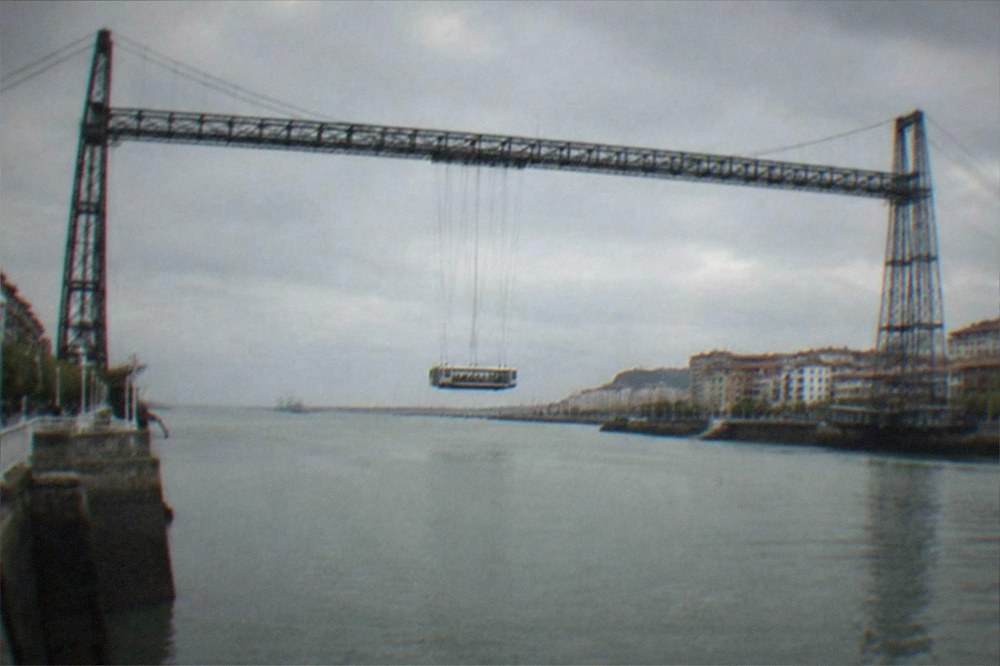 A tall steel transporter bridge spanning a wide estuary with a small gondola suspended beneath it