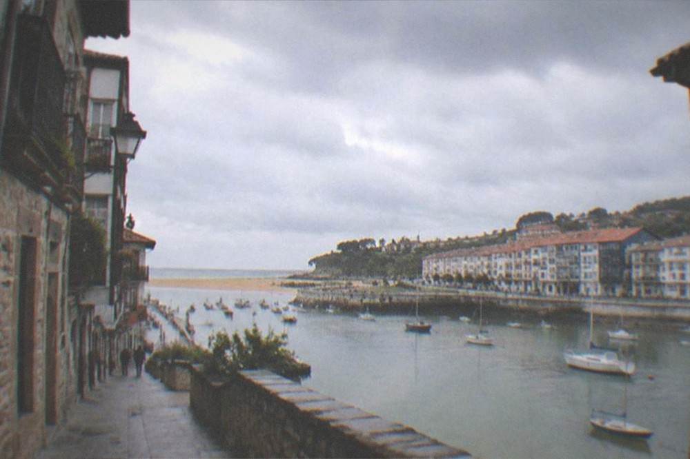 A narrow old-town street with stone buildings and hanging signs in a Basque coastal town