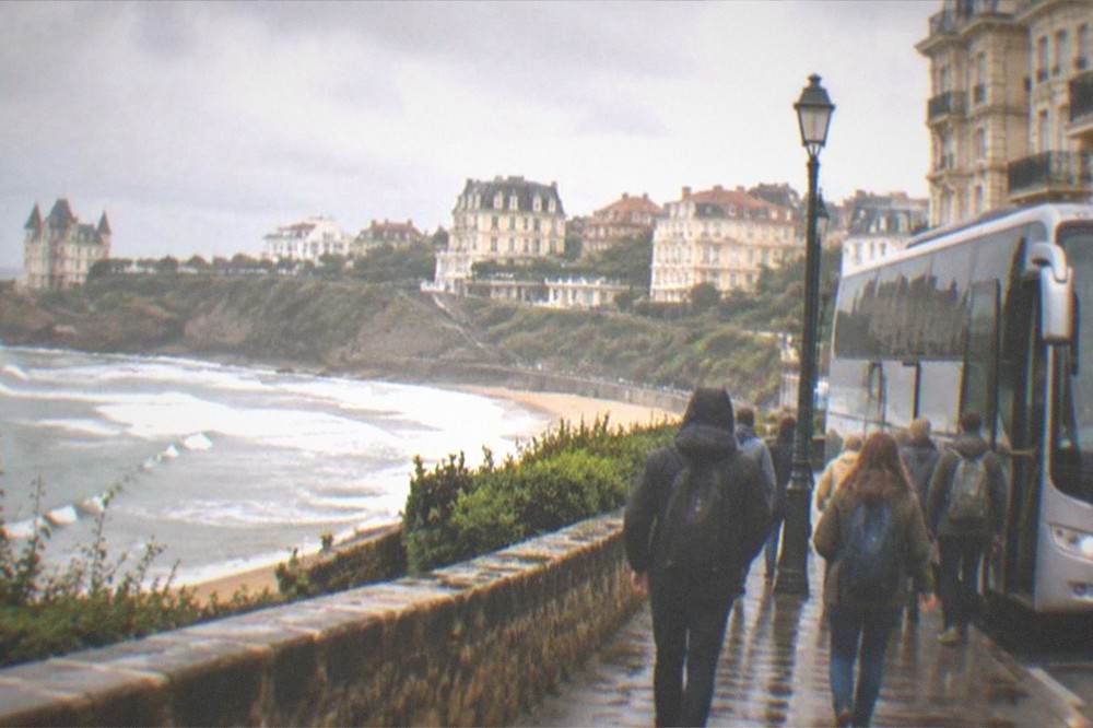 Travelers with small backpacks walking toward a waiting tour coach in a European city street