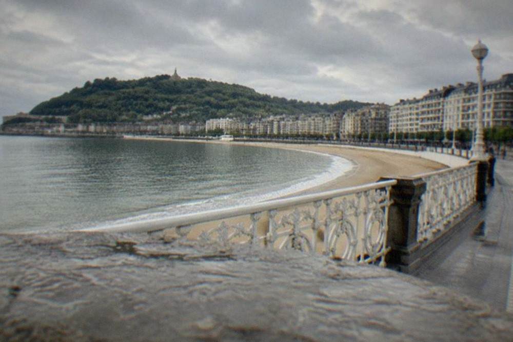 White apartment buildings and railings along a wide curved beach promenade on a bright morning