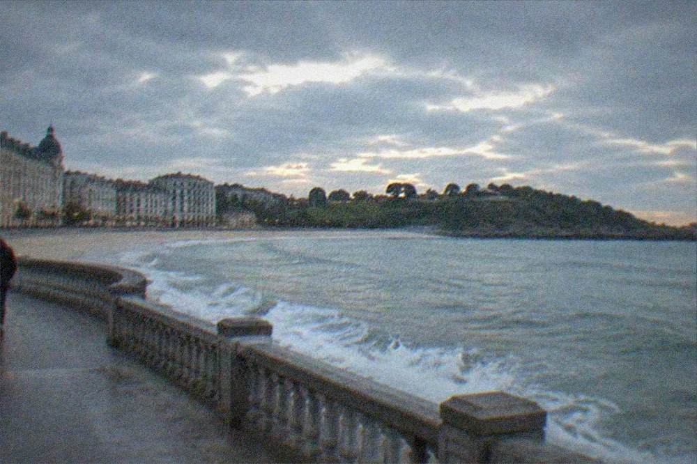 Waves breaking against a stone seafront balustrade under a grey Atlantic sky