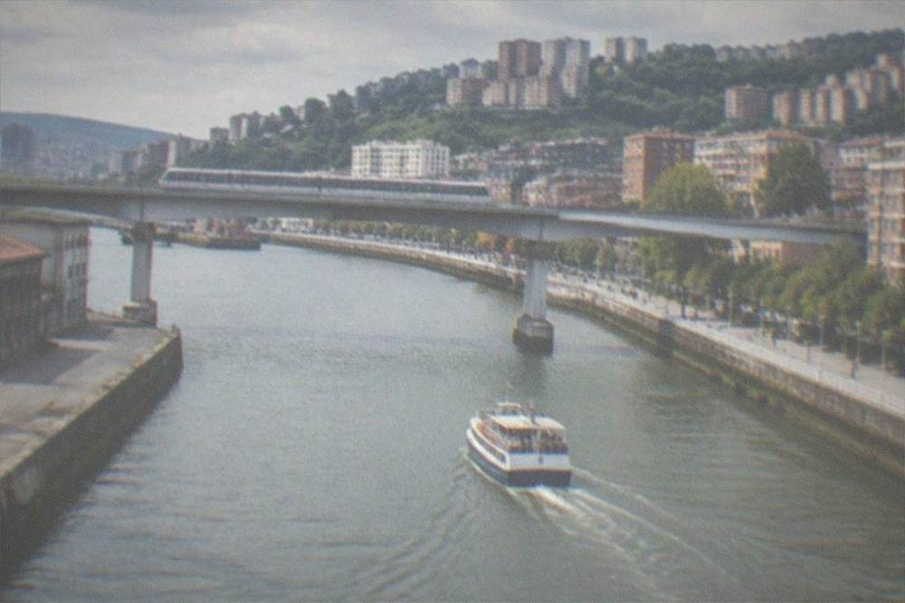 A metro train crossing a bridge over the Nervion estuary with apartment blocks on the hillsides