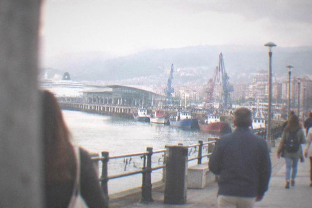 Passengers walking along a waterfront promenade toward the old town streets of Bilbao in the late afternoon