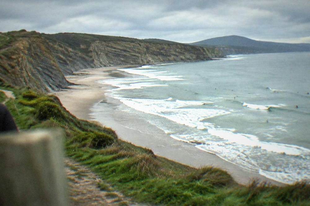 Green clifftop path above the sea with the sandy beach curving below