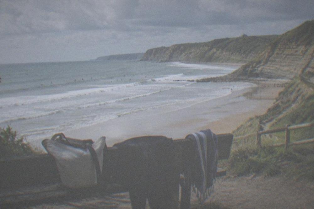 Beach bag, wetsuit and towel on a bench facing the sea