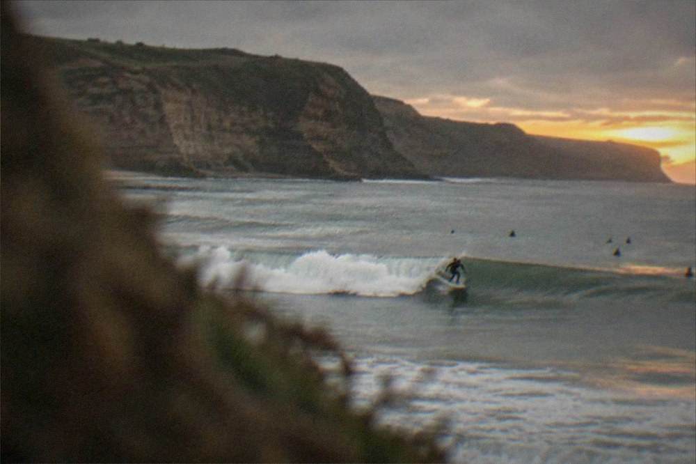 Surfer riding a wave at sunset with cliffs in the background