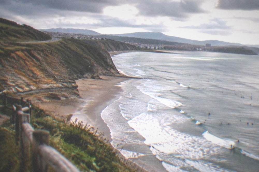 Coastal road winding along green cliffs above the sea toward a distant town