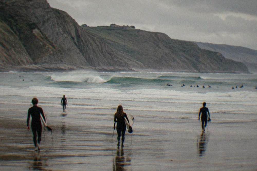 Surfers in wetsuits walking across wet sand toward the sea at Sopelana