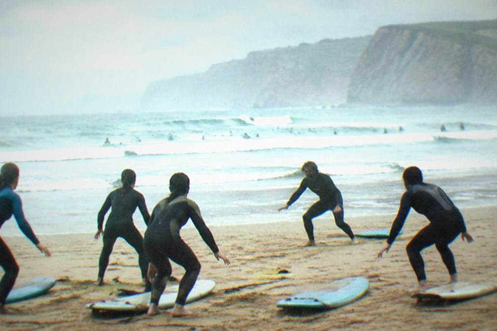 Surf instructor demonstrating a pop-up stance on the sand with a group of learners