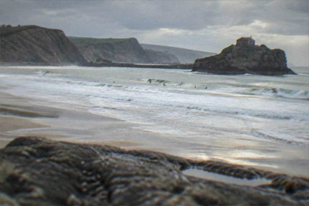 Rocky islet with a stone hermitage connected by a narrow causeway and steps seen from the coast
