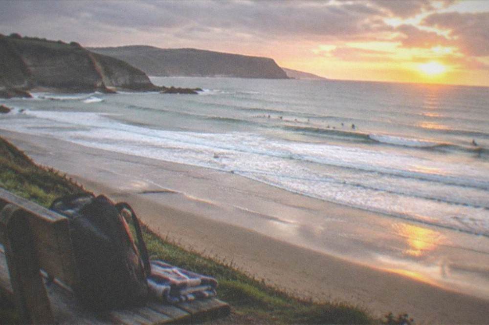 Backpack and folded towel on a wooden beach bench facing the sea at sunset